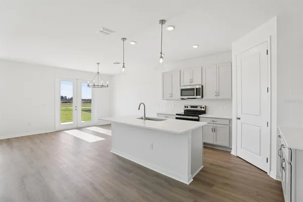 a kitchen with stainless steel appliances granite countertop a stove a sink a refrigerator and white cabinets with wooden floor