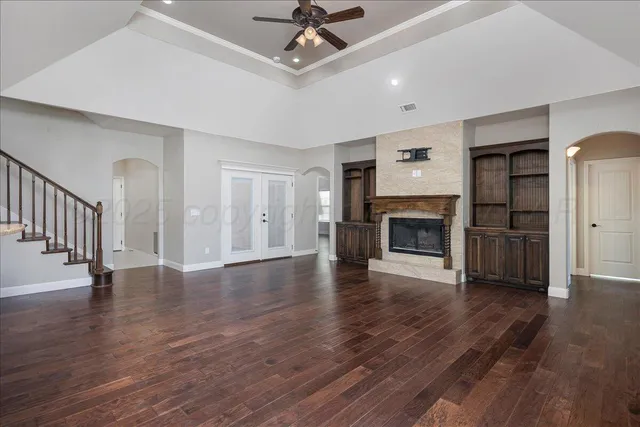 a view of a livingroom with wooden floor a fireplace a ceiling fan and windows