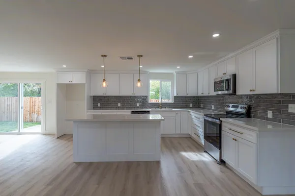 a large kitchen with stainless steel appliances granite countertop a stove a sink dishwasher and a oven with white cabinets
