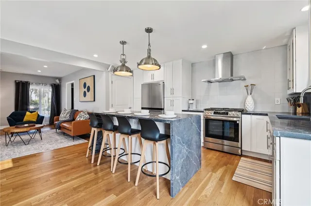 a kitchen with stainless steel appliances kitchen island granite countertop a stove a sink a dining table and chairs with wooden floor