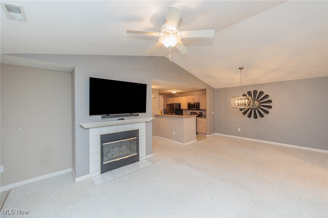 28360 Center Ridge Road, Unit 2210 Westlake, OH 44145 - Photo 10 of 45 Unfurnished living room featuring light carpet, lofted ceiling, a fireplace, and ceiling fan with notable chandelier