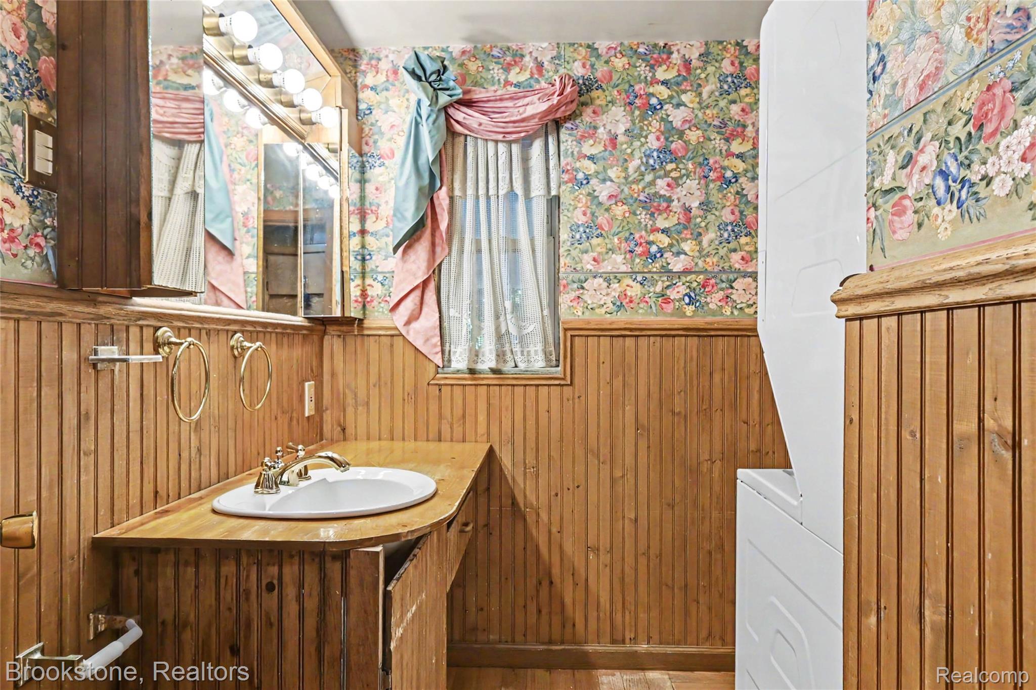 416 East Maple Street Mason, MI 48854 - Photo 12 of 18 Bathroom featuring wood paneling, a single basin vanity with a polished chrome faucet, a mirrored medicine cabinet with integrated lighting, and floral wallpaper