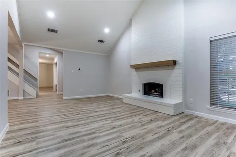 a view of an empty room with wooden floor fireplace and a window