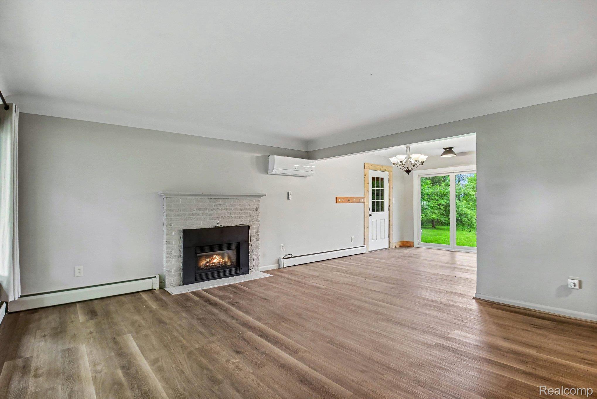 2487 North Lapeer Road Lapeer, MI 48446 - Photo 4 of 16 Spacious room featuring wood-finish flooring, a white brick fireplace with a black insert, and a wall-mounted mini-split unit