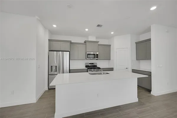 a kitchen with stainless steel appliances a refrigerator stove a sink a oven and white cabinets with wooden floor