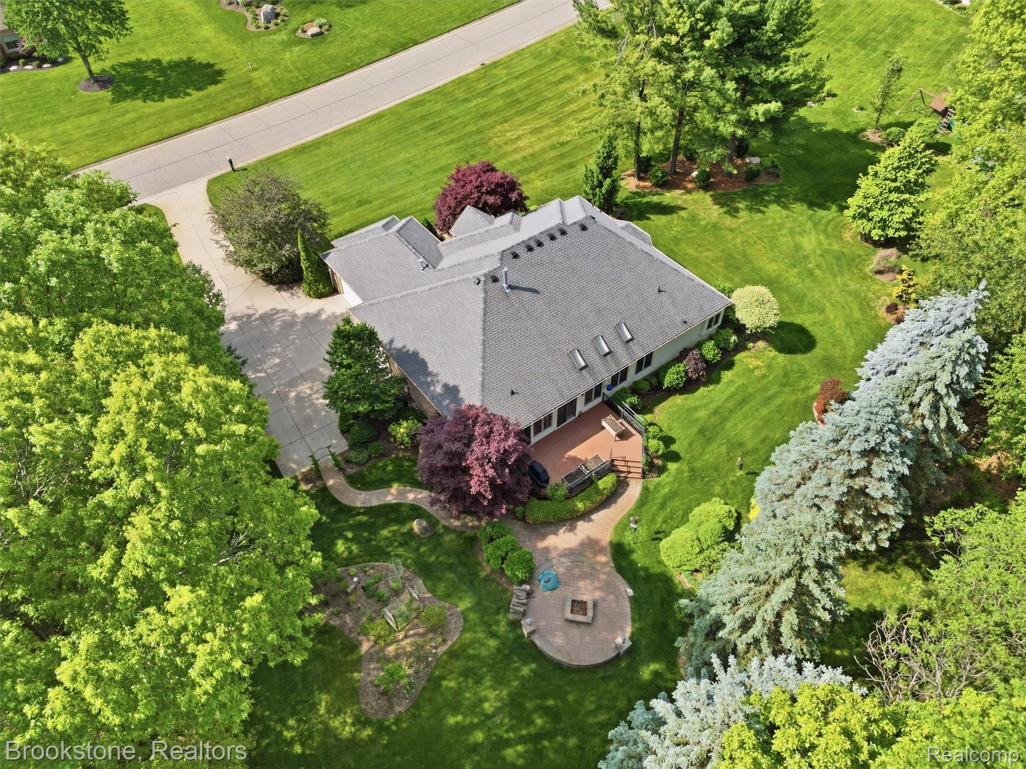 9523 Quail Ridge Run Brighton, MI 48114 - Photo 11 of 50 Expansive property featuring a paved driveway, mature trees, a multi-level deck, a winding stone pathway, and a circular patio with a fire pit