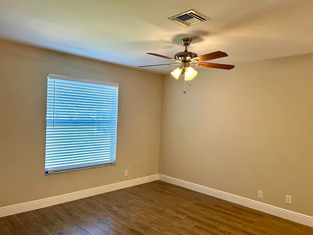 an empty room with wooden floor fan and windows