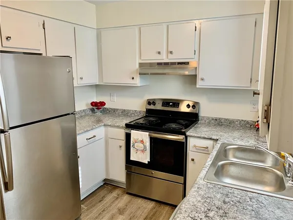 a kitchen with granite countertop a refrigerator sink stove and white cabinets