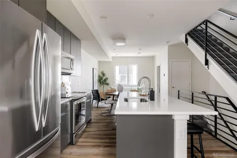 a kitchen with stainless steel appliances granite countertop a refrigerator a sink dishwasher a stove and a dining table with wooden floor