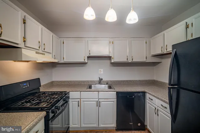 a kitchen with granite countertop a refrigerator stove and white cabinets