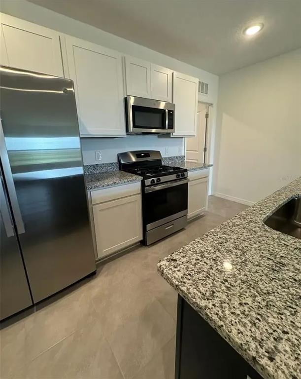 15074 Windflower Alley Winter Garden, FL 34787 - Photo 2 of 18 a kitchen with stainless steel appliances kitchen island granite countertop a stove a sink and a microwave