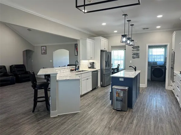 a open kitchen with a sink dishwasher a dining table chairs with wooden floor and cabinets