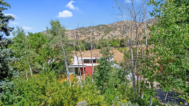 510 Spring Creek Road Providence, UT 84332 - Photo 82 of 97 Modern architecture with a red accent panel and expansive windows, surrounded by mature trees and natural landscaping