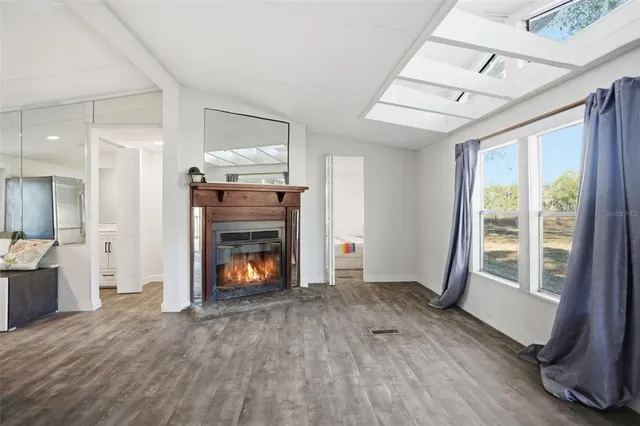 a view of an empty room with wooden floor fireplace and a window