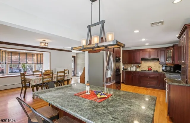 a kitchen with stainless steel appliances granite countertop a stove top oven a dining table and chairs with wooden floor