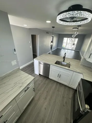 a view of a kitchen with kitchen island a stove a sink wooden floor and living room view