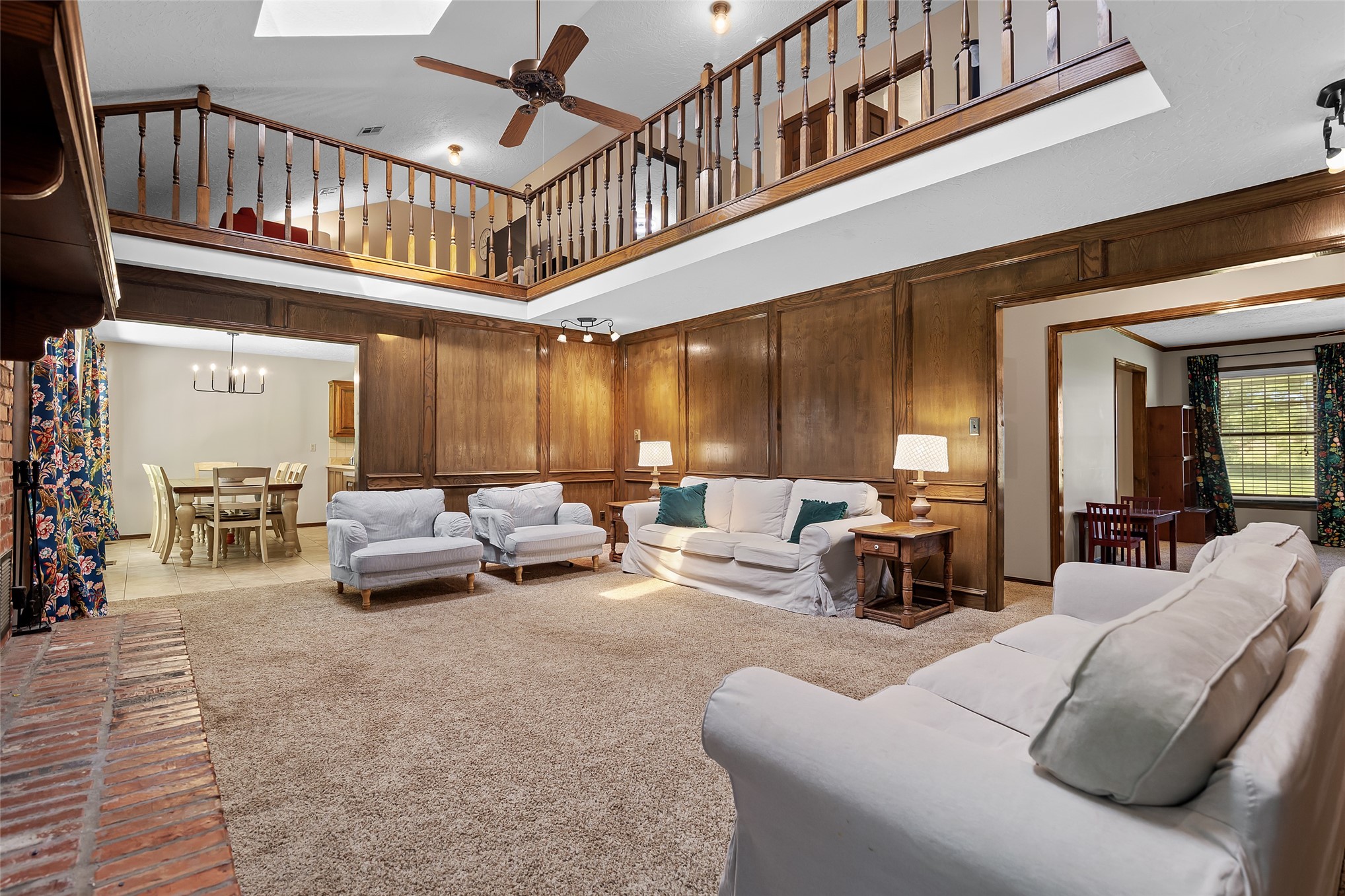 9644 19th Road Nowata, OK 74048 - Photo 4 of 36 Spacious living area featuring wood-paneled walls, a double-height ceiling, a second-story balcony with wood railings, a ceiling fan, and a skylight
