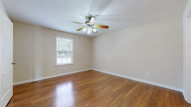 an empty room with wooden floor chandelier fan and windows