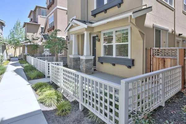 a view of a white house with a small yard and wooden fence