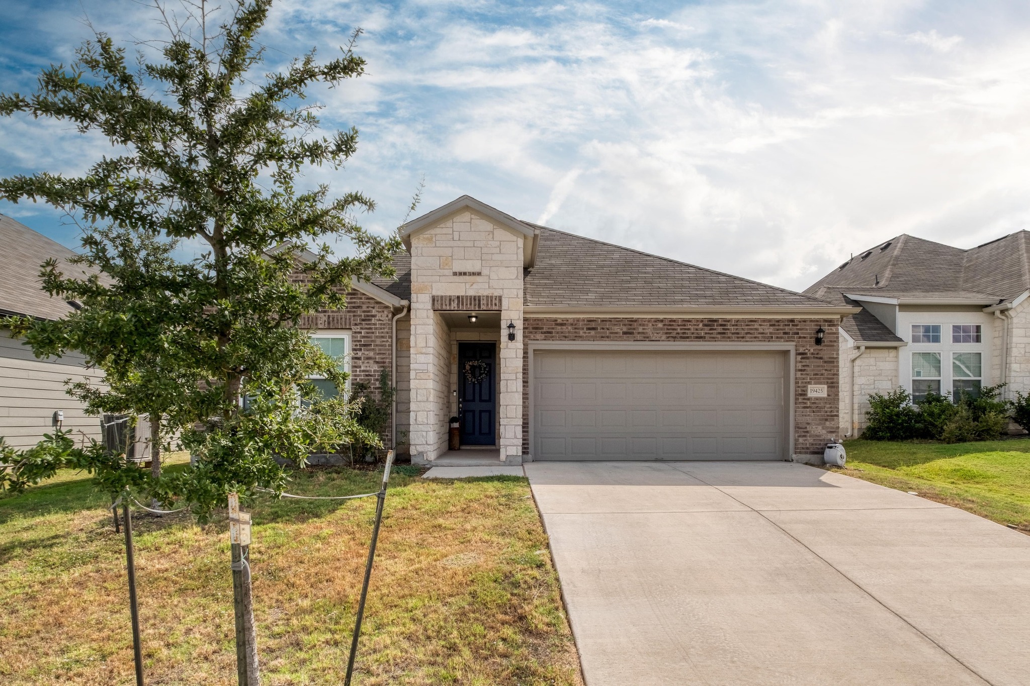View of front of home featuring driveway, an attached garage, stone siding, a front yard, and brick siding