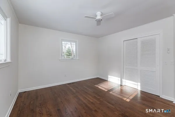 an empty room with wooden floor chandelier fan and windows