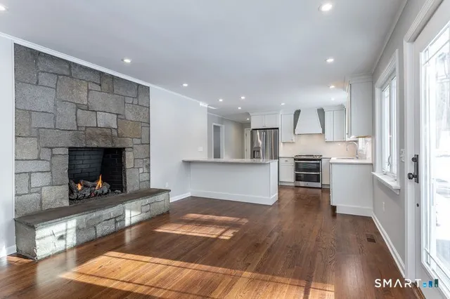 a living room with stainless steel appliances furniture a fireplace and wooden floor