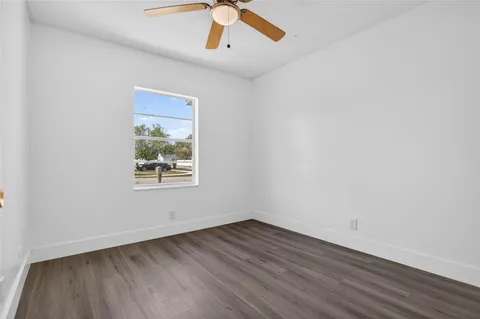 an empty room with wooden floor chandelier fan and windows