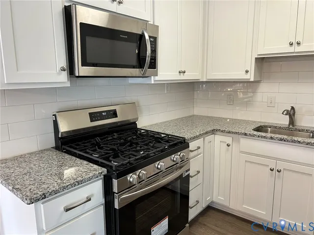 a kitchen with granite countertop white cabinets stainless steel appliances and wooden floor