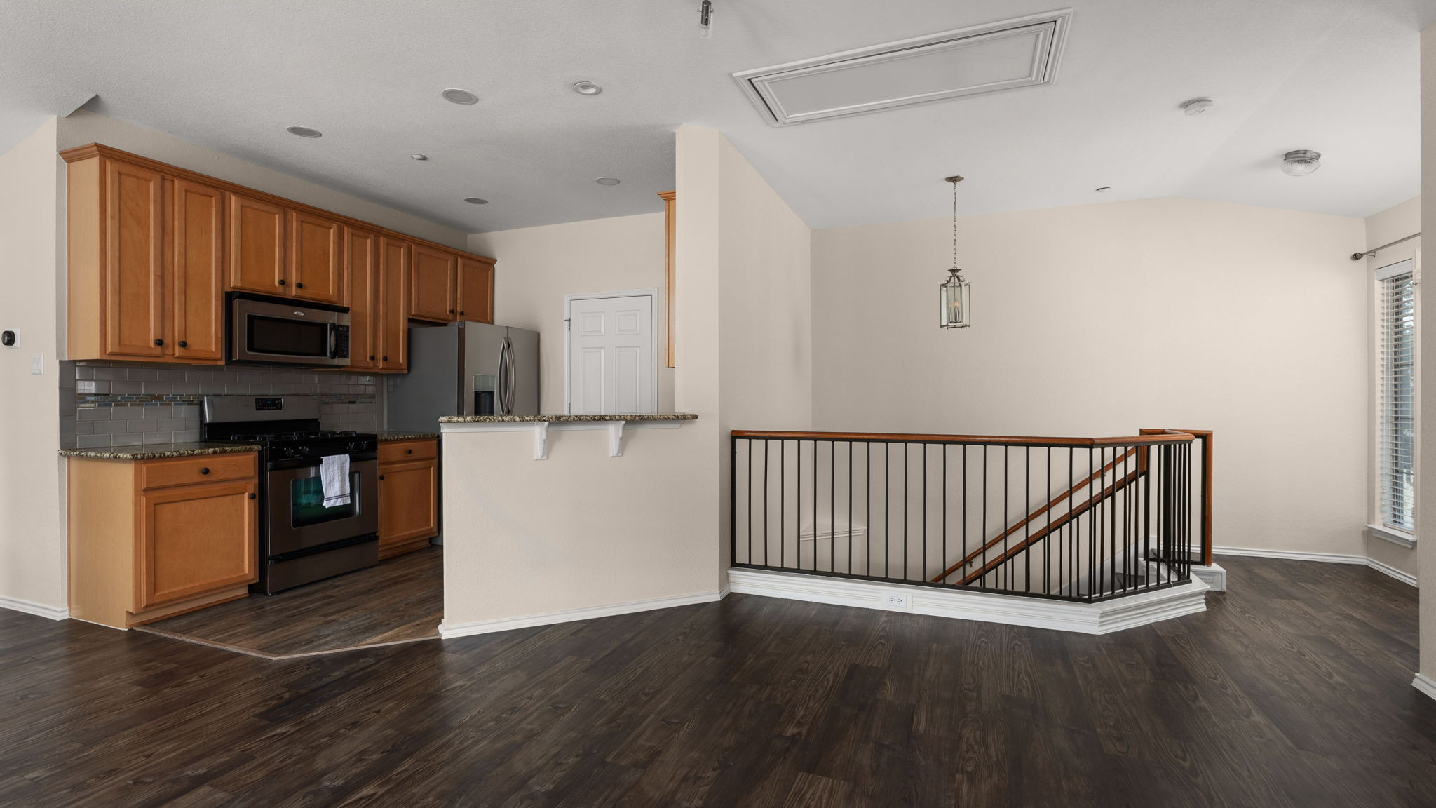 14815 Avery Ranch Boulevard, Unit 1401 Austin, TX 78717 - Photo 2 of 38 Open-concept living area featuring wood-finish flooring, a kitchen with stainless steel appliances, granite countertops, and wood cabinetry, and a staircase with a wrought iron railing and wood handrail