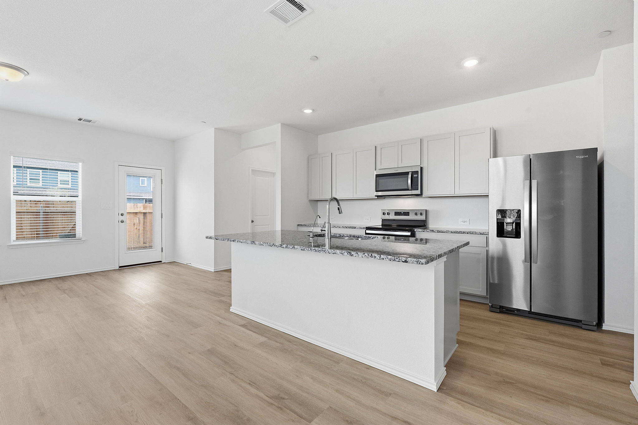 164 Cinnabar Lane, Unit 5 Kyle, TX 78640 - Photo 7 of 21 Open-concept kitchen and living area featuring wood-finish flooring, a kitchen island with granite countertops, stainless steel appliances, white cabinetry, and recessed lighting