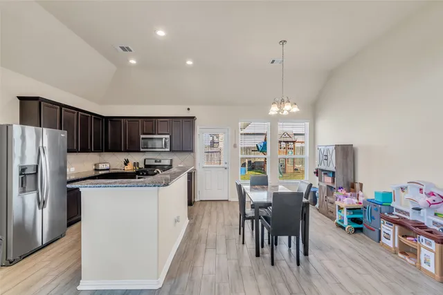 a kitchen with stainless steel appliances a dining table chairs stove refrigerator and cabinets