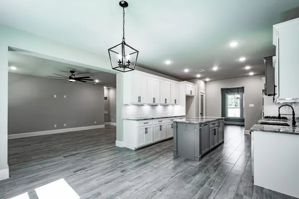 a kitchen with stainless steel appliances granite countertop a sink a stove a refrigerator and white cabinets with wooden floor