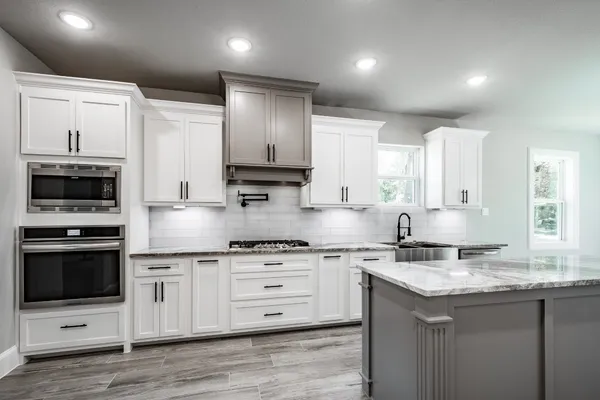 a kitchen with stainless steel appliances granite countertop a sink stove a refrigerator and white cabinets with wooden floor