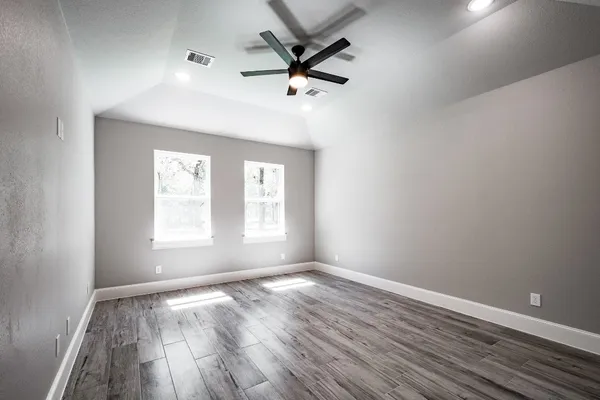 an empty room with wooden floor fan and windows
