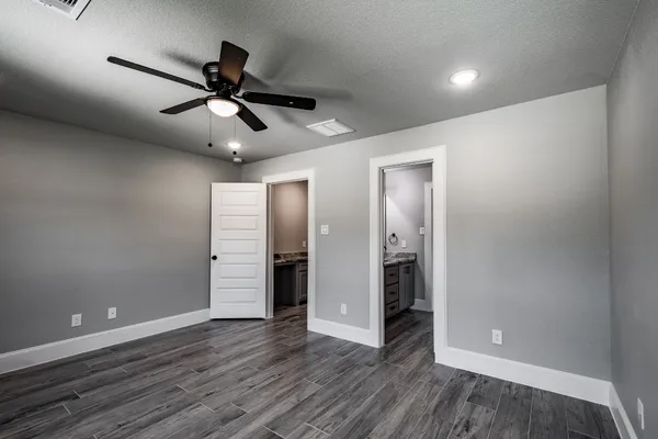 a view of an empty room with wooden floor and a ceiling fan