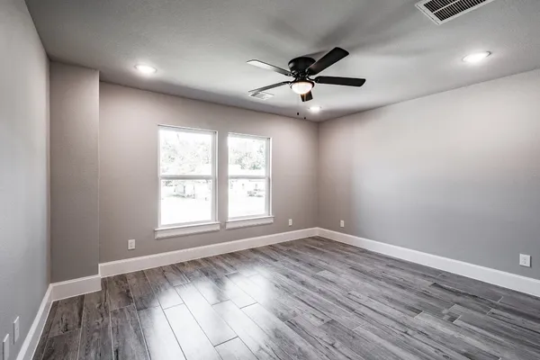 an empty room with wooden floor fan and windows