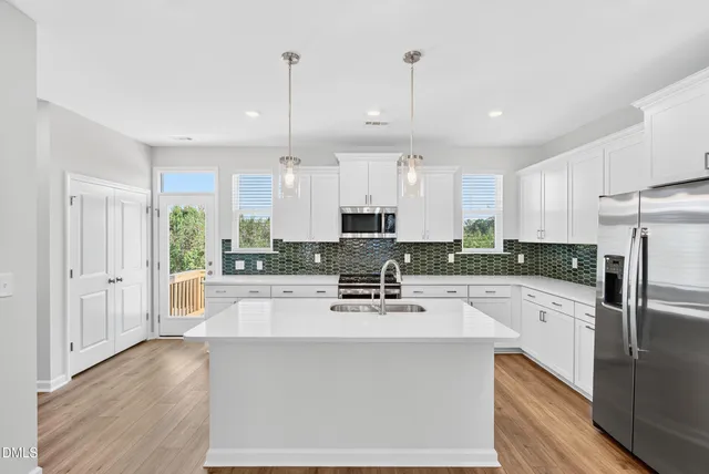 a kitchen with stainless steel appliances a refrigerator a stove a sink and white cabinets with wooden floor