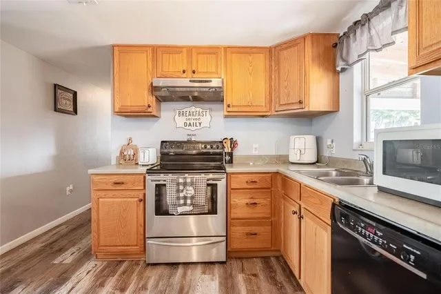 a kitchen with stainless steel appliances granite countertop a refrigerator a stove and a sink with wooden floor