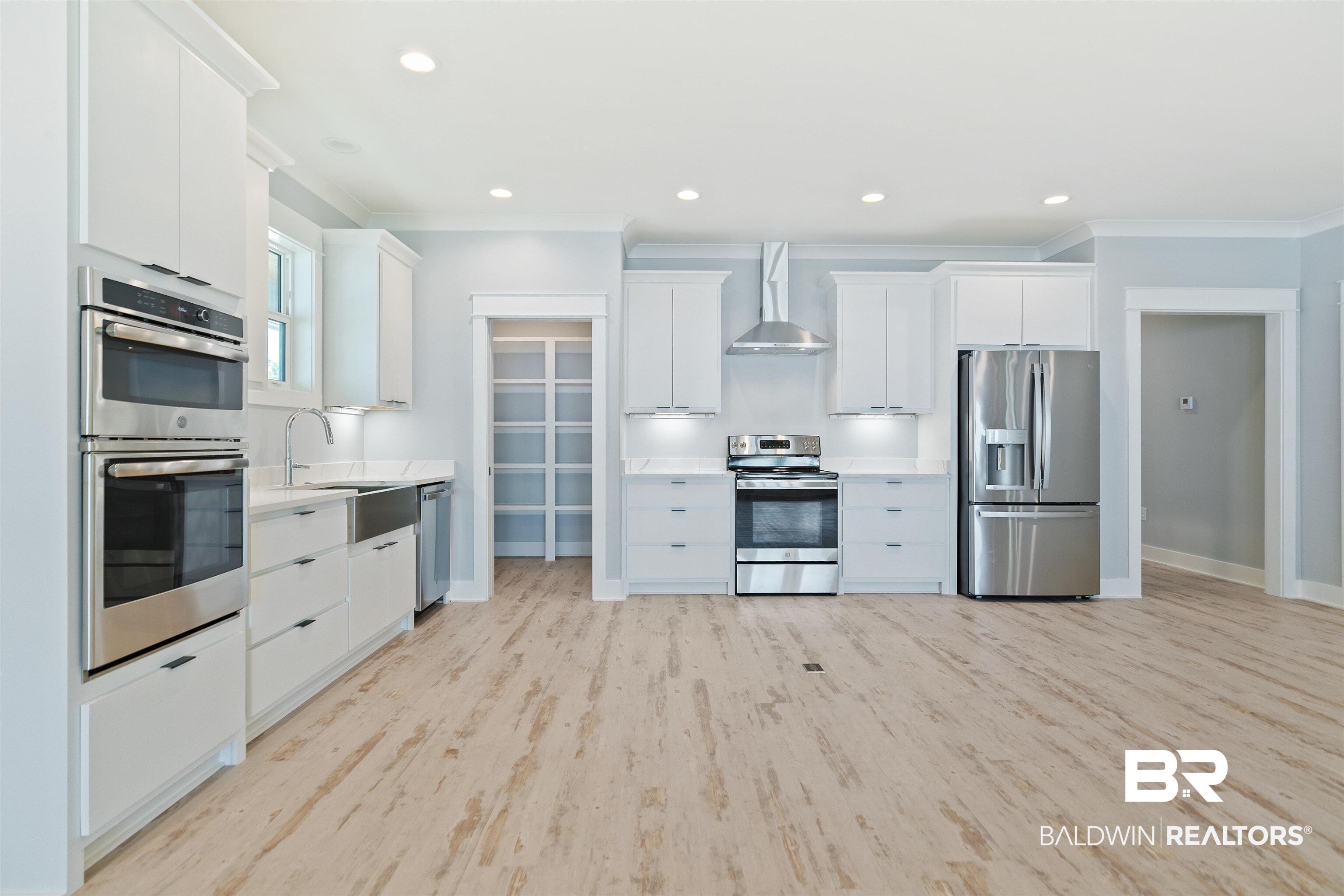 10507 County Road 1 Fairhope, AL 36532 - Photo 12 of 59 Kitchen with white cabinetry, wall chimney exhaust hood, sink, light hardwood / wood-style floors, and appliances with stainless steel finishes