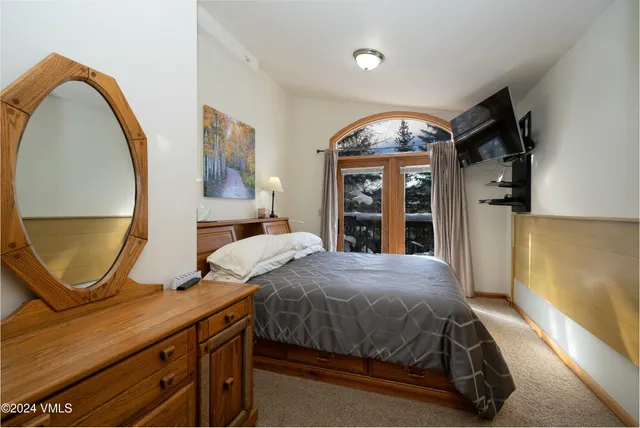 a bedroom with a bed a mirror on the dresser and a large window