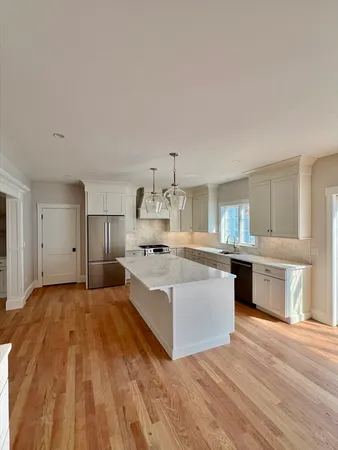 a large white kitchen with a stove a sink dishwasher and a refrigerator with wooden floor