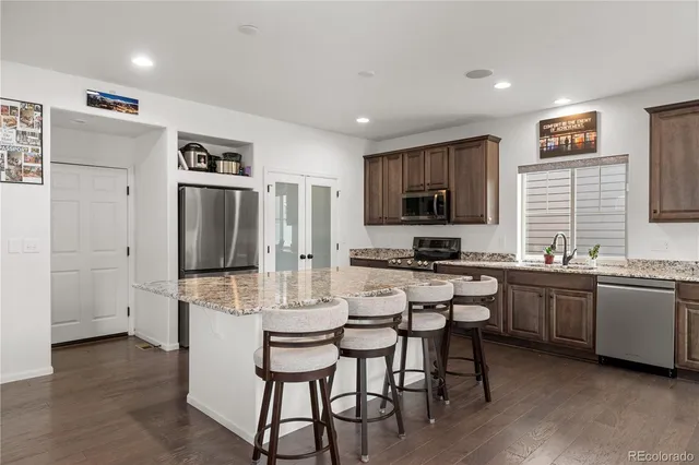 a kitchen with stainless steel appliances granite countertop a stove a sink dishwasher a refrigerator and a dining table with wooden floor