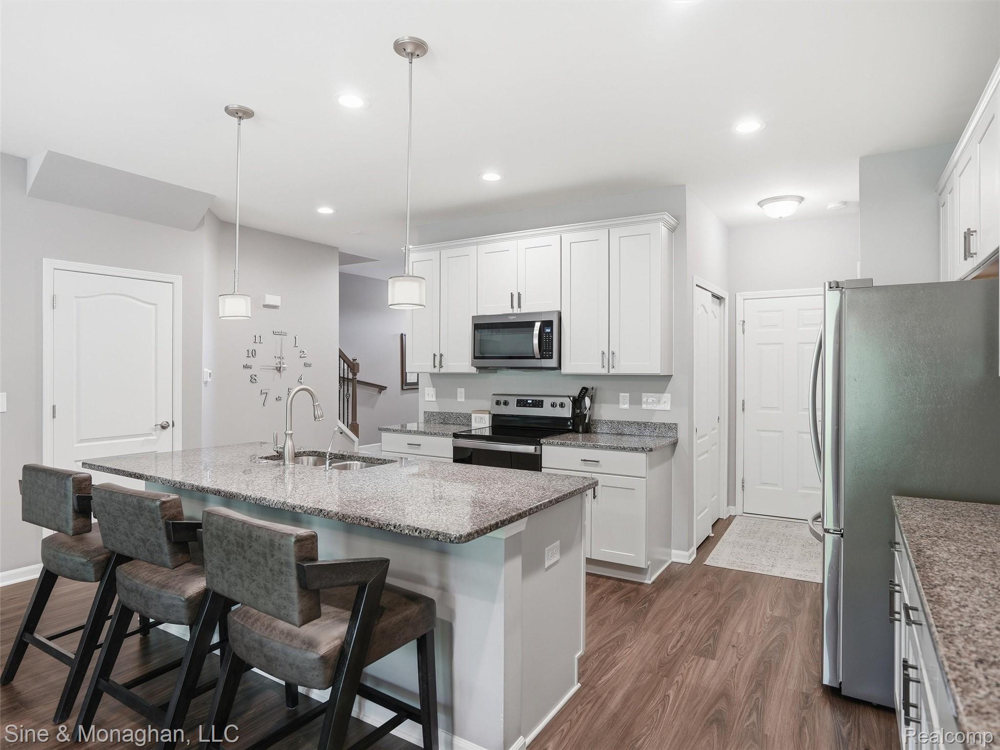 24827 Ivy Road Novi, MI 48375 - Photo 7 of 38 Modern kitchen featuring a granite-topped island with an undermount sink, pendant lighting, stainless steel appliances, white cabinetry, and wood-finish flooring