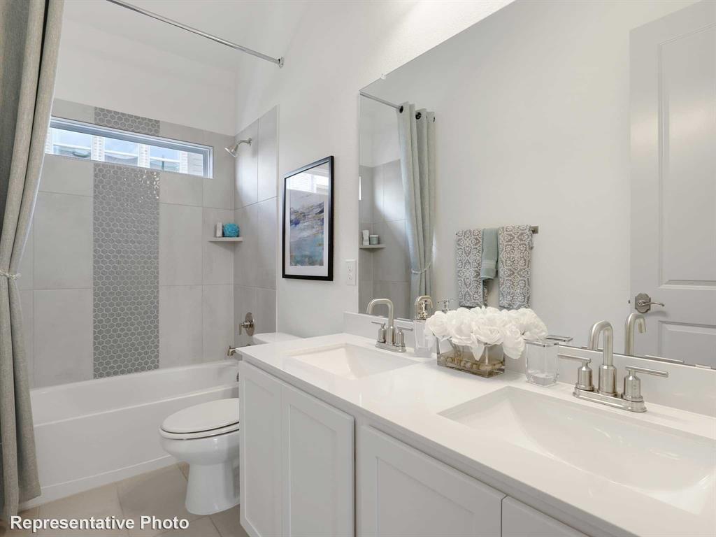 2204 Ridgecrest Lane Anna, TX 75409 - Photo 12 of 17 Bathroom featuring a dual vanity with undermount sinks and brushed nickel fixtures, a full-width mirror, a tub/shower combination with light-toned tiling and a mosaic accent, and a horizontal transom window