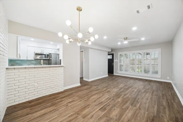 a view of an empty room with wooden floor and kitchen view
