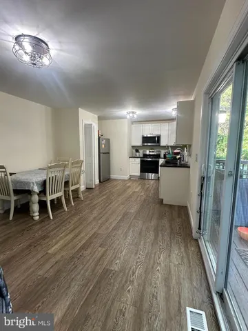 a living room with stainless steel appliances furniture wooden floor and a kitchen view