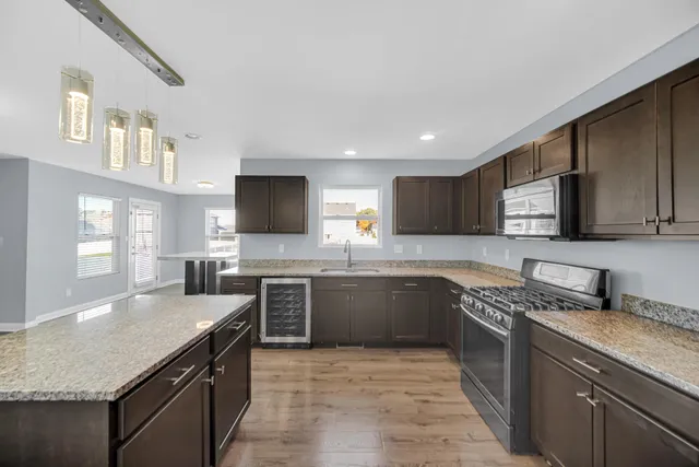 a large kitchen with stainless steel appliances granite countertop a stove top oven a sink dishwasher a dining table and chairs with wooden floor