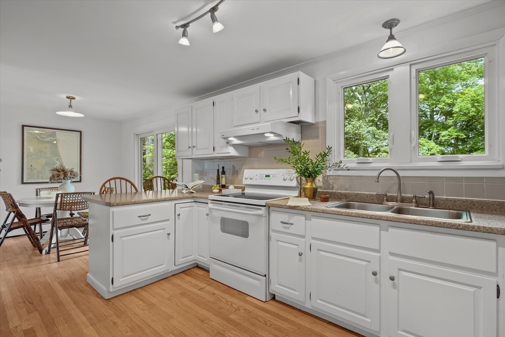 50 Middle Road Amesbury, MA 01913 - Photo 6 of 30 a kitchen with white cabinets a sink dishwasher a dining table and chairs with wooden floor