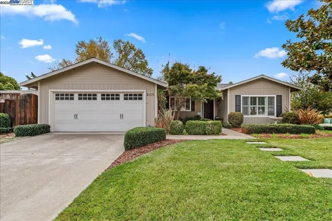 a view of a house with a yard plants and a large tree