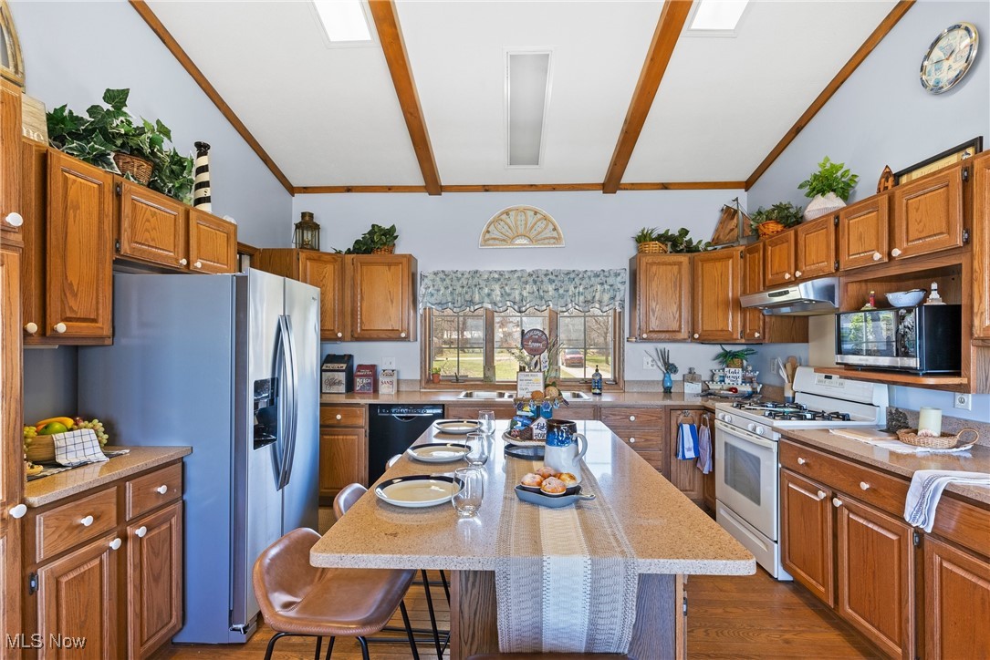 1122 Lake Road Conneaut, OH 44030 - Photo 22 of 50 Kitchen with under cabinet range hood, vaulted ceiling with beams, a kitchen bar, and appliances with stainless steel finishes